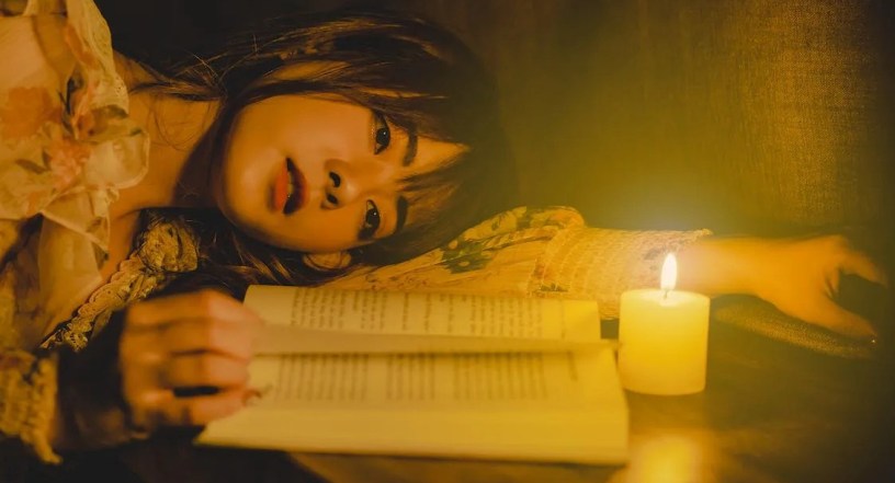 woman lying down on table with wax candle and reading